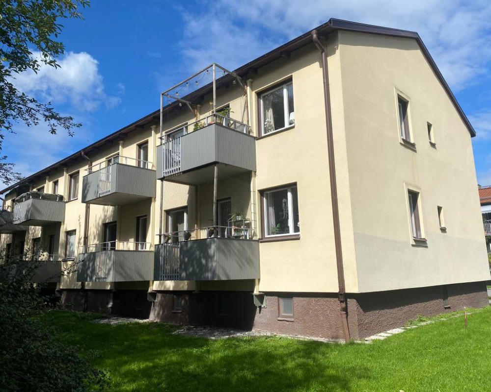 Ljusgult flerbostadshus med balkonger och en grön gräsmatta i solsken