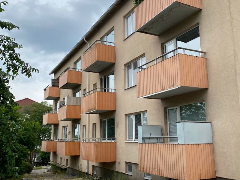 Flerbostadshus i tre våningar med orange balkonger och grönska