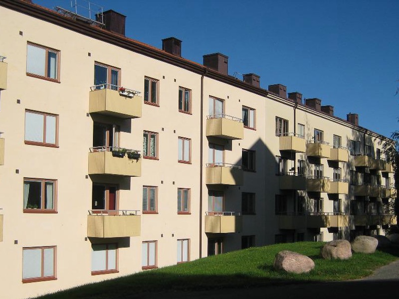 Ljust flerbostadshus med balkonger och en gräsbacke med stora stenar i sol